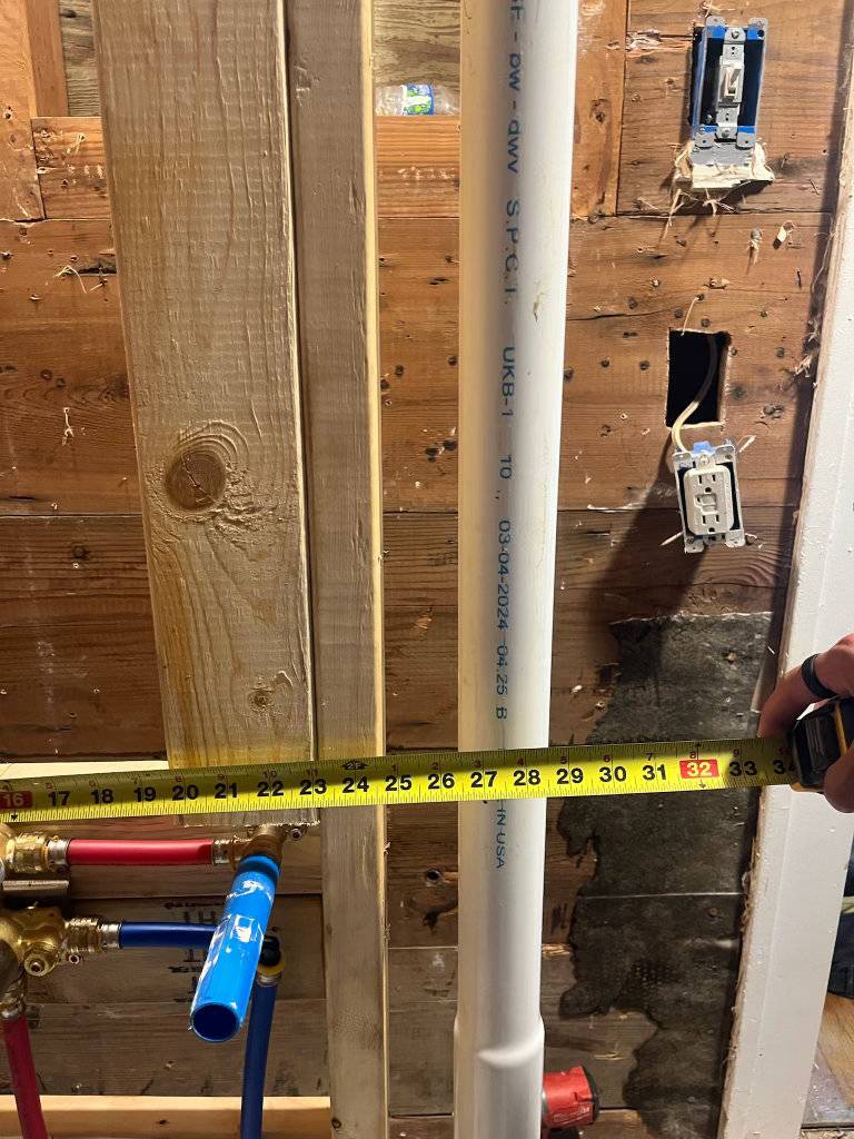 Licensed plumber measuring rough-in supply and drain piping during a Stephenville, TX plumbing installation